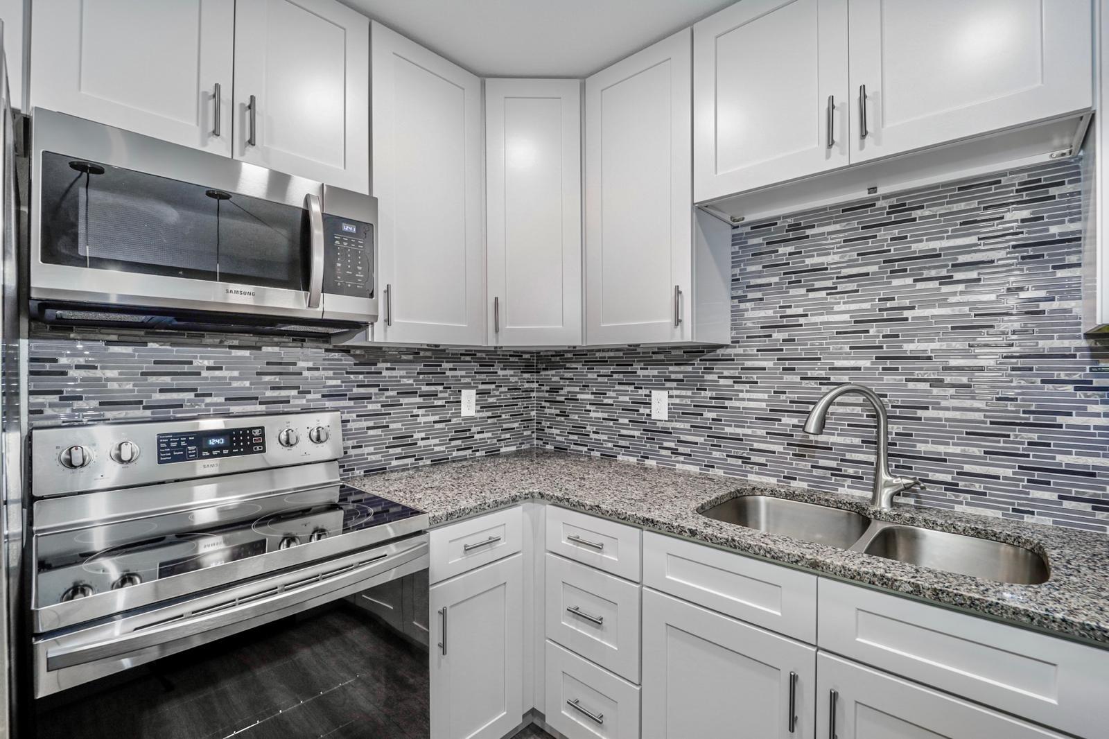 White shaker kitchen with grey mosaic backsplash and granite — The Bayfront Residence, Palm Coast, FL