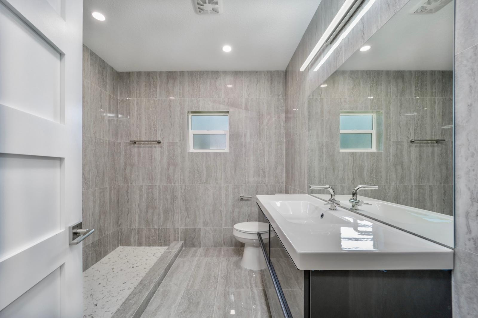 Walk-in shower with travertine tile and double sink trough — The Travertine Suite, Palm Coast, FL